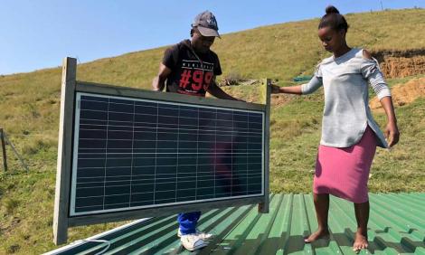 Image description: A man and a woman hold a solar panel on a roof