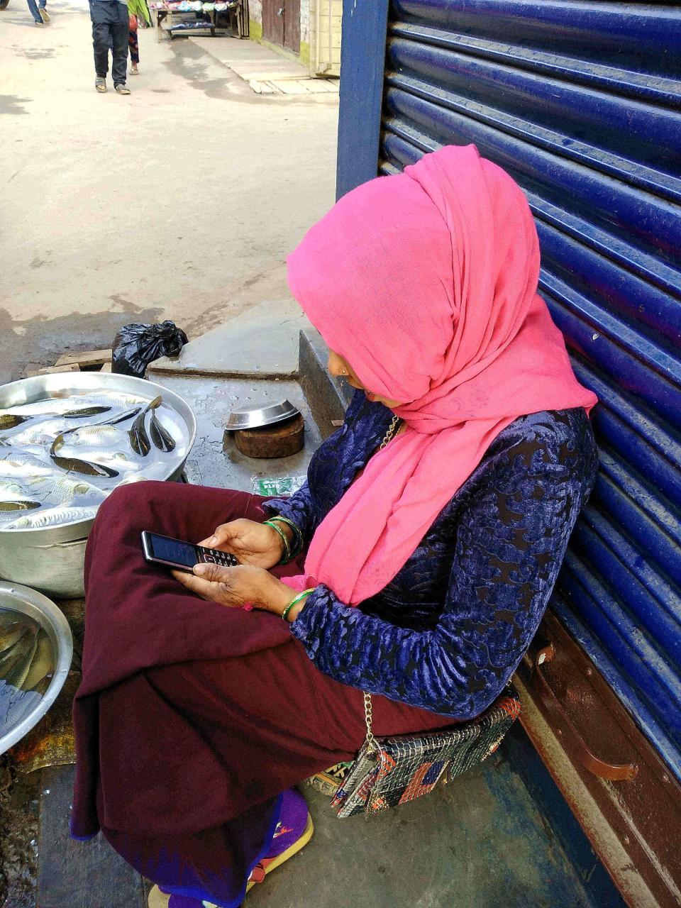 Image description: woman with mobile phone seated outside shop