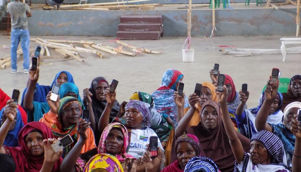 Image description: Photo of women holding up basic mobile phones