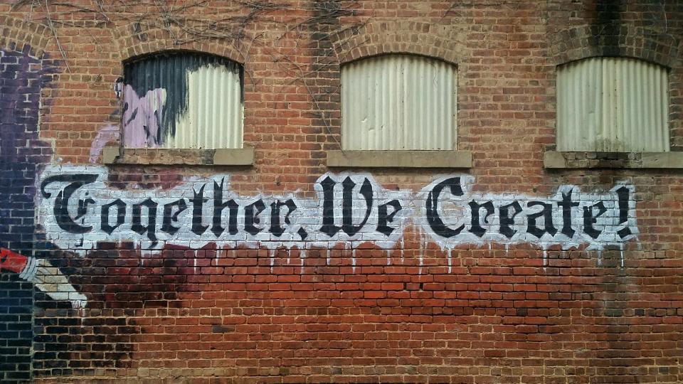 Graffiti saying "Together We Create" on a brick wall